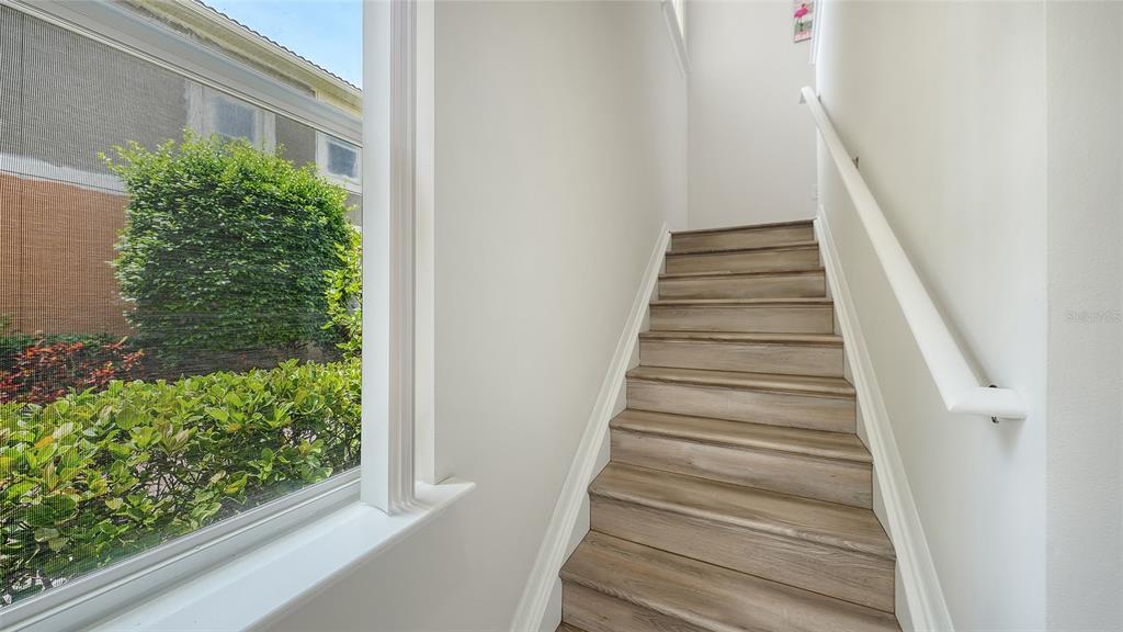 A staircase with wood-look steps and a white handrail sits beside a large window — 7843 MOONSTONE DRIVE UNIT 24-202, SARASOTA, FL