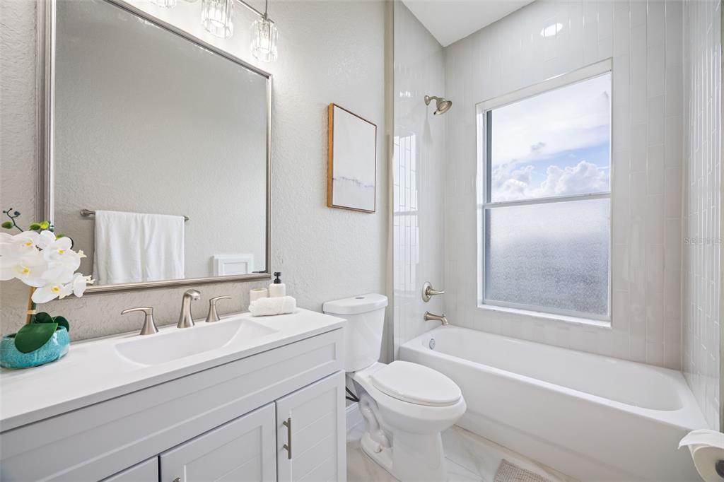 A modern bathroom features a white vanity, a toilet, and a bathtub with a window — 1340 APOLLO BEACH BOULEVARD S, APOLLO BEACH, FL