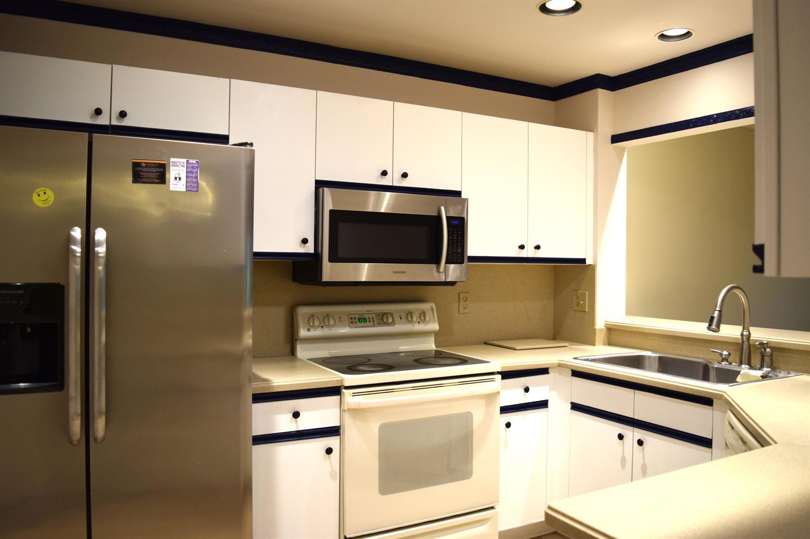 A kitchen features white cabinets with blue trim, stainless steel appliances, and beige countertops — 9416 Boca River Circle # 9416, Boca Raton FL 33434, BOCA RATON, FL