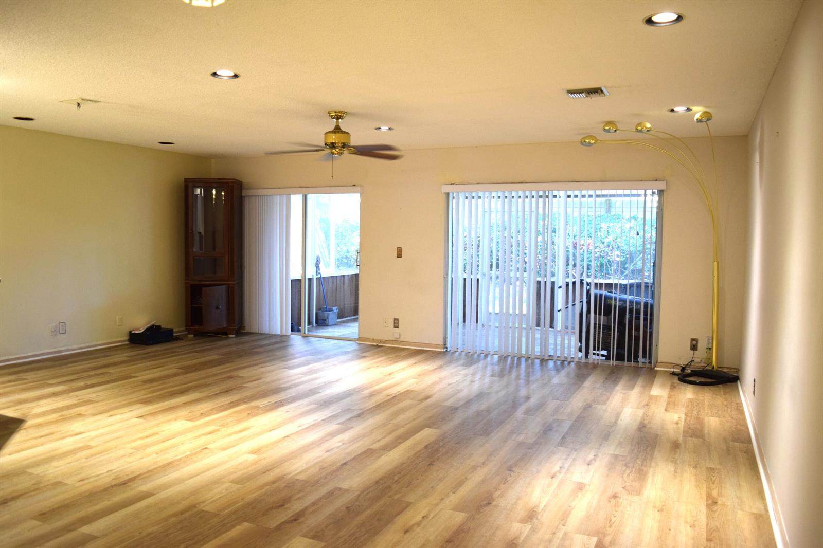A spacious living room features light wood-look flooring, a ceiling fan, and sliding glass doors — 9416 Boca River Circle # 9416, Boca Raton FL 33434, BOCA RATON, FL