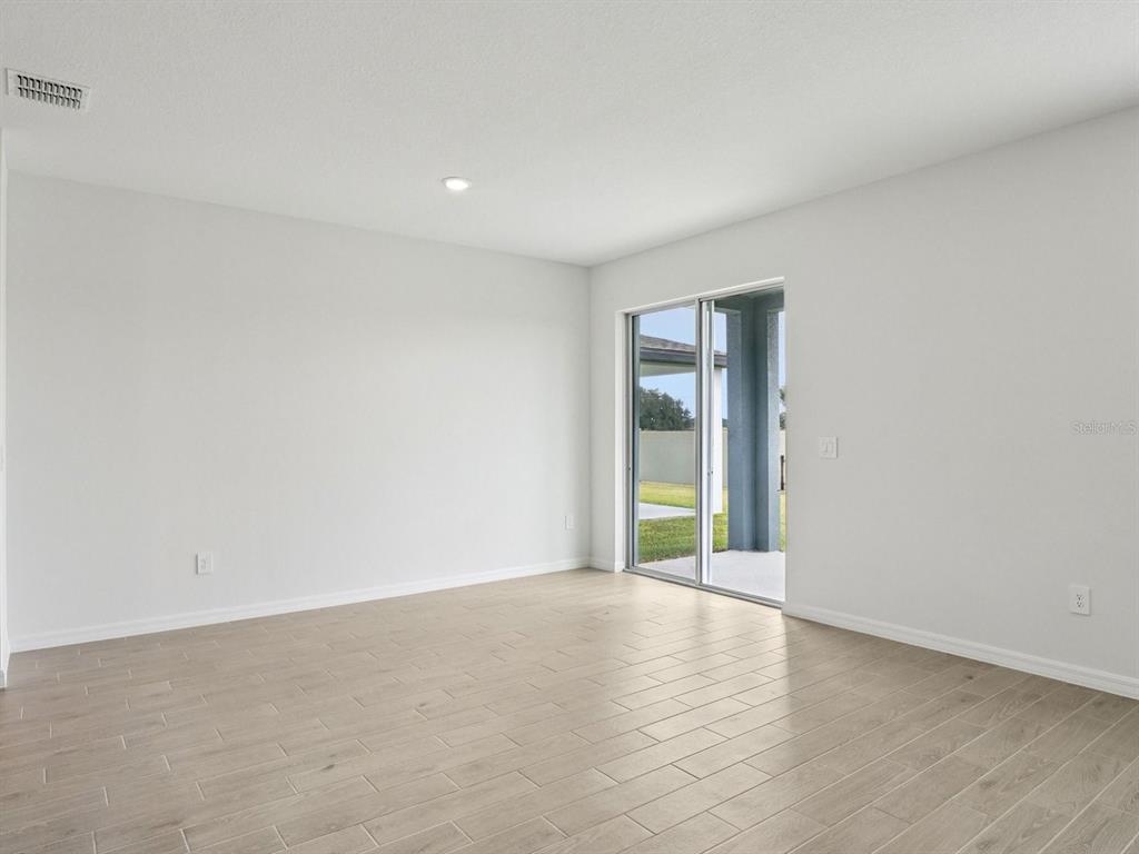 An empty room with light wood-look tile flooring, white walls, and a sliding glass door — 128 OUTBACK HIDEAWAY AVENUE, NOKOMIS, FL