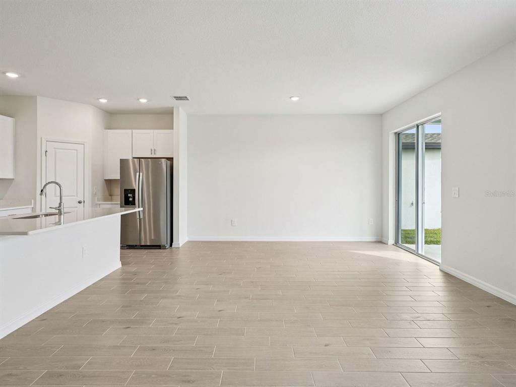 A bright, open-concept kitchen and dining area features light wood-look tile flooring and sliding doors — 128 OUTBACK HIDEAWAY AVENUE, NOKOMIS, FL