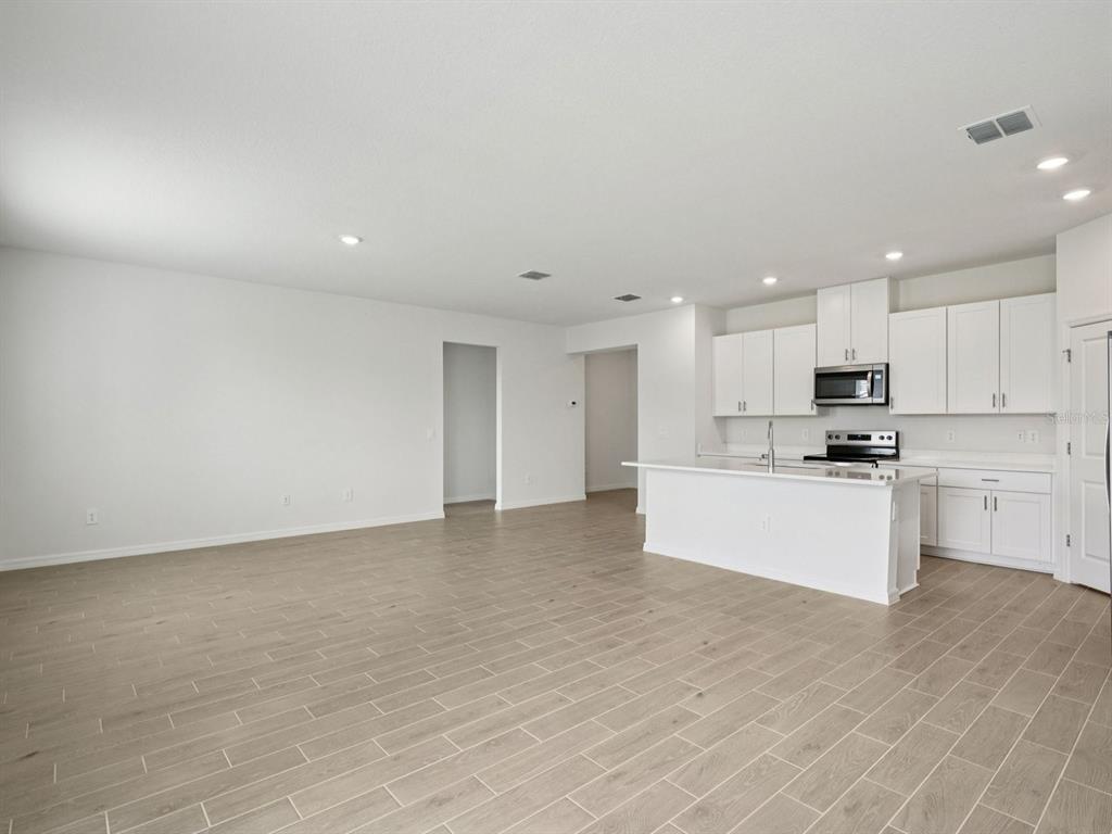 An open-concept kitchen and living area featuring white cabinetry, a central island, and tile flooring — 128 OUTBACK HIDEAWAY AVENUE, NOKOMIS, FL