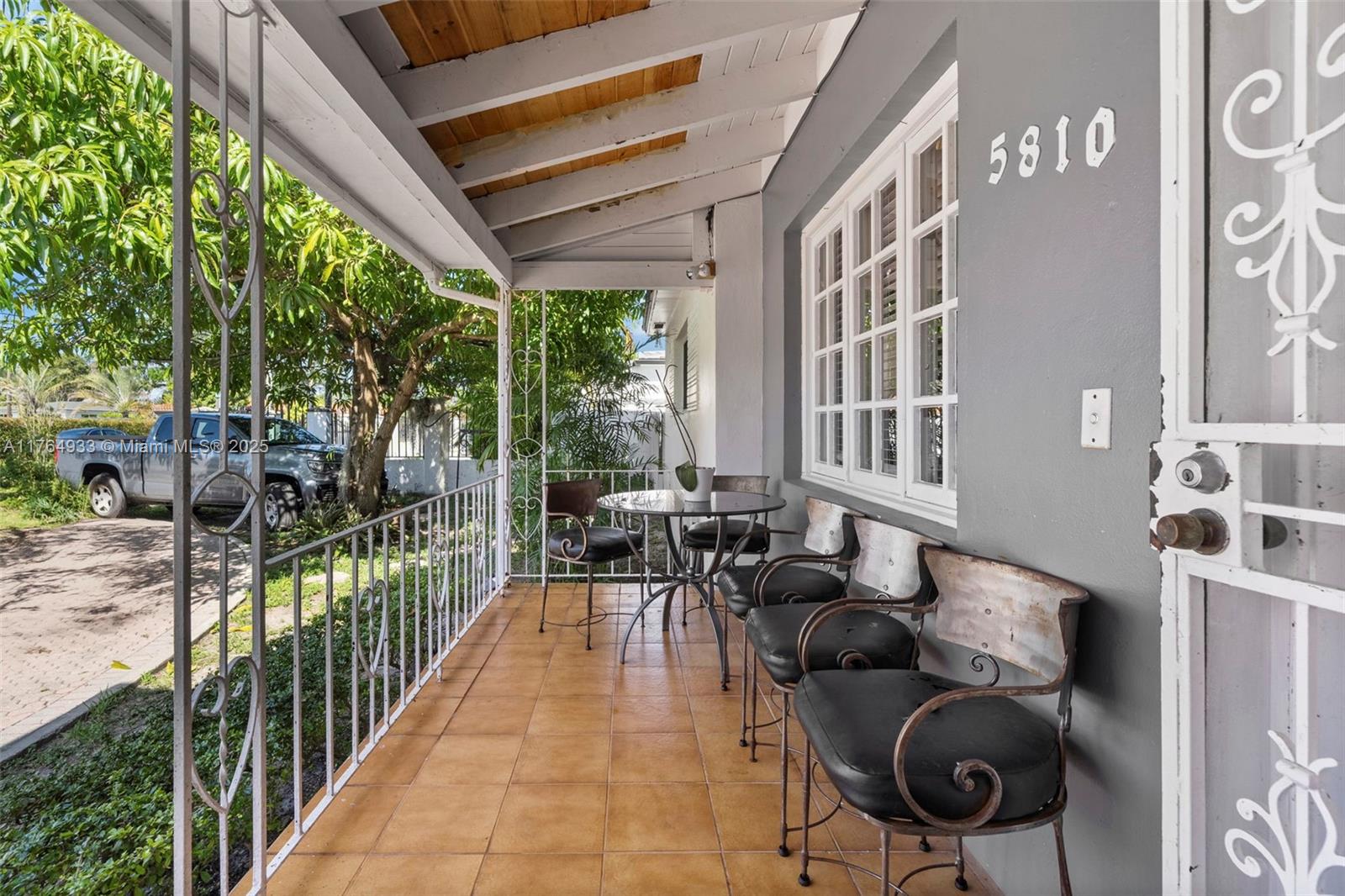 A covered porch features tiled flooring, wrought iron furniture, and a gray exterior wall — 5810 SW 22nd St, Miami FL 33155, MIAMI, FL