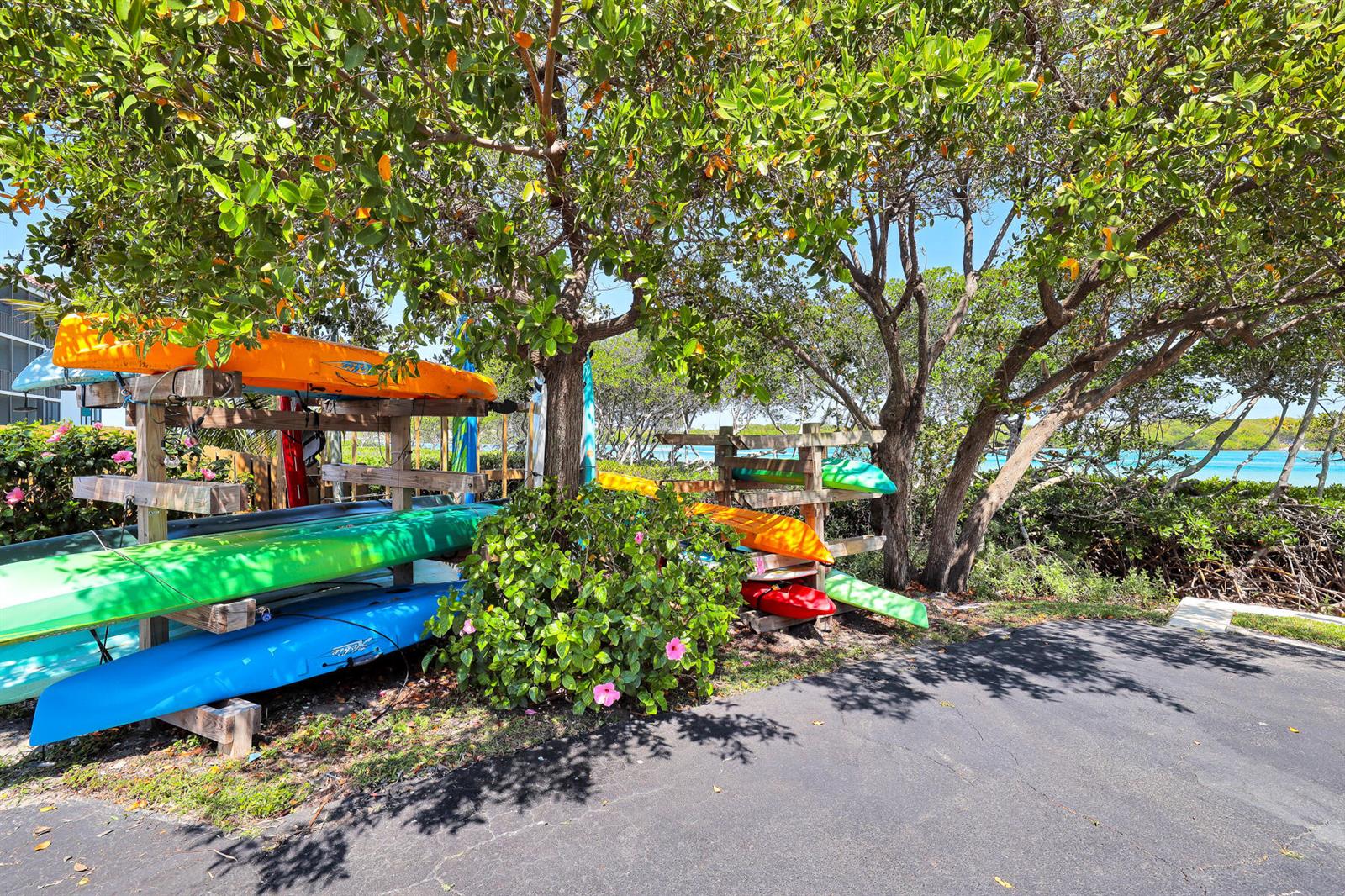 A wooden rack holds several colorful kayaks under trees near a paved path and water — 100 Waterway Road # A303, Jupiter FL 33469, JUPITER, FL