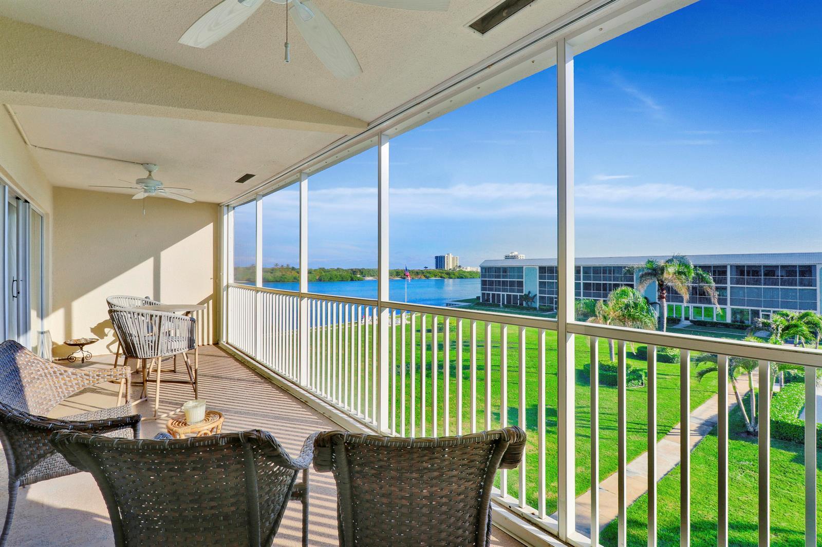 A screened-in balcony features wicker furniture, ceiling fans, and a view of a grassy lawn — 100 Waterway Road # A303, Jupiter FL 33469, JUPITER, FL