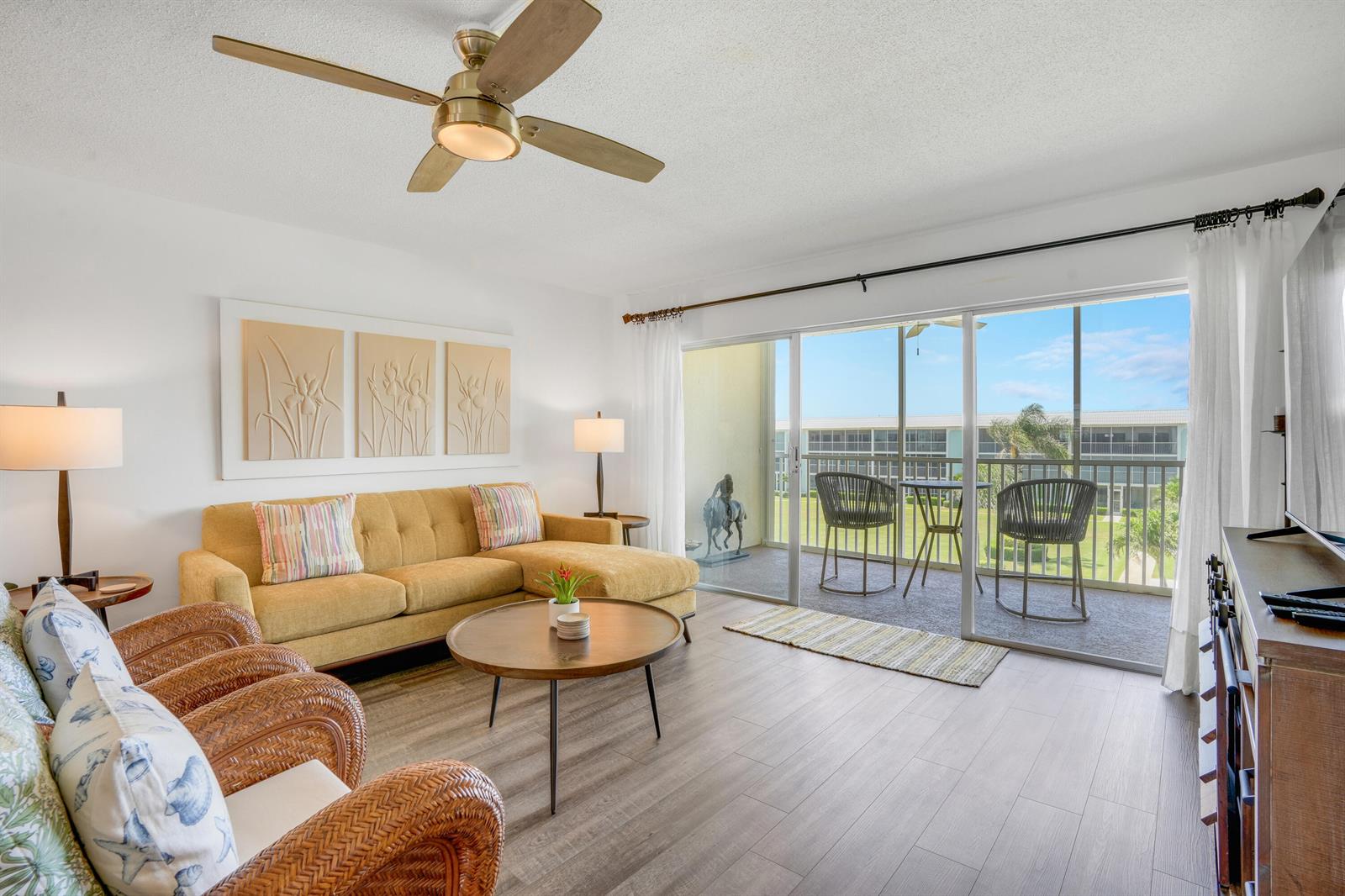 A living room with a yellow sectional, wicker chairs, and a sliding door to a balcony — 100 Waterway Road # A303, Jupiter FL 33469, JUPITER, FL