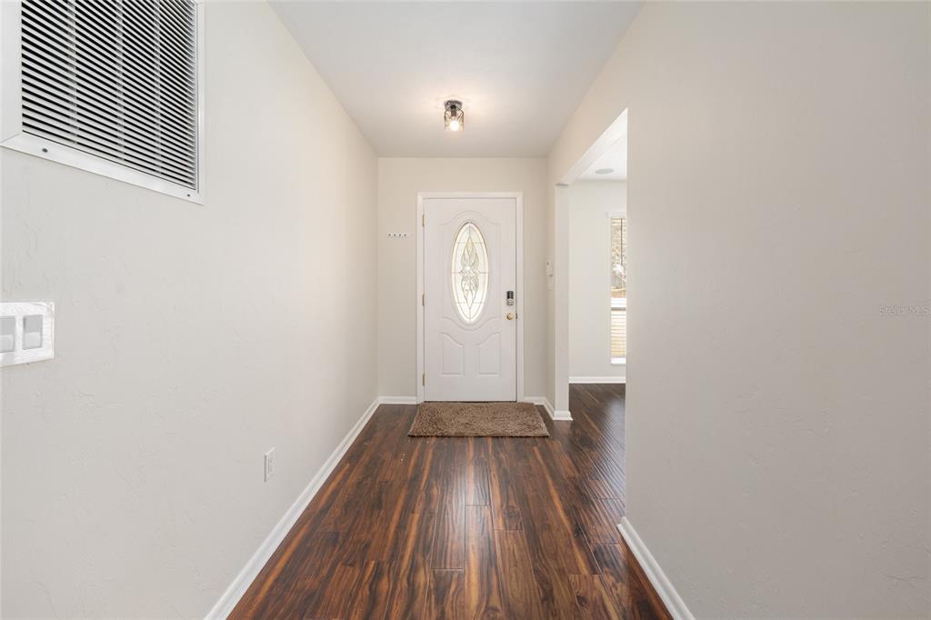 An entryway features dark wood-look flooring, light walls, and a white front door with glass — 8205 SW 44TH TERRACE, GAINESVILLE, FL