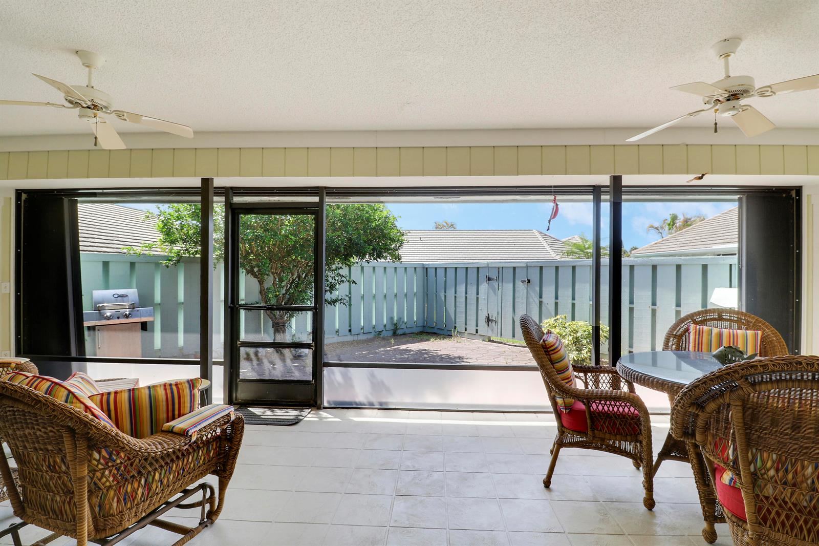 A screened-in patio features wicker furniture, ceiling fans, tiled flooring, and a fenced backyard view — 1127 E Seminole Avenue # 15b, Jupiter FL 33477, JUPITER, FL