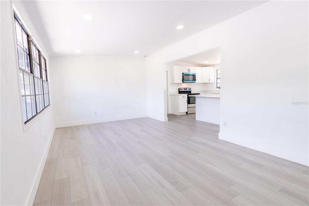 A bright, open-concept living area with light wood-look flooring leads into a white kitchen — 4112 W FAIRVIEW HEIGHTS, TAMPA, FL