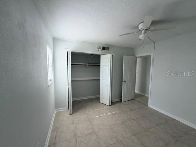 A bedroom with light gray walls, tile flooring, a ceiling fan, and an open closet — 5521 BAY BOULEVARD UNIT 101, PORT RICHEY, FL