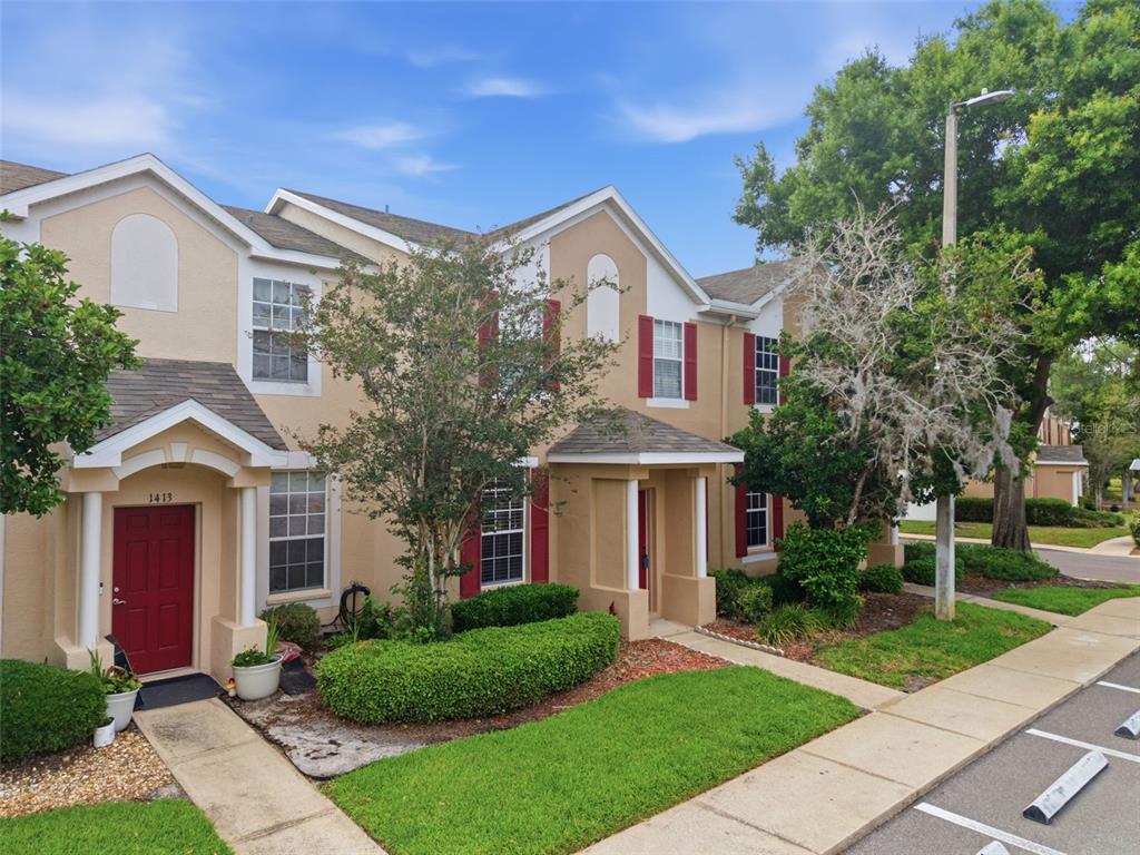 An exterior view of two adjacent townhomes with tan stucco walls, red doors, and red shutters — 1415 SEDGWICK DRIVE, WESLEY CHAPEL, FL