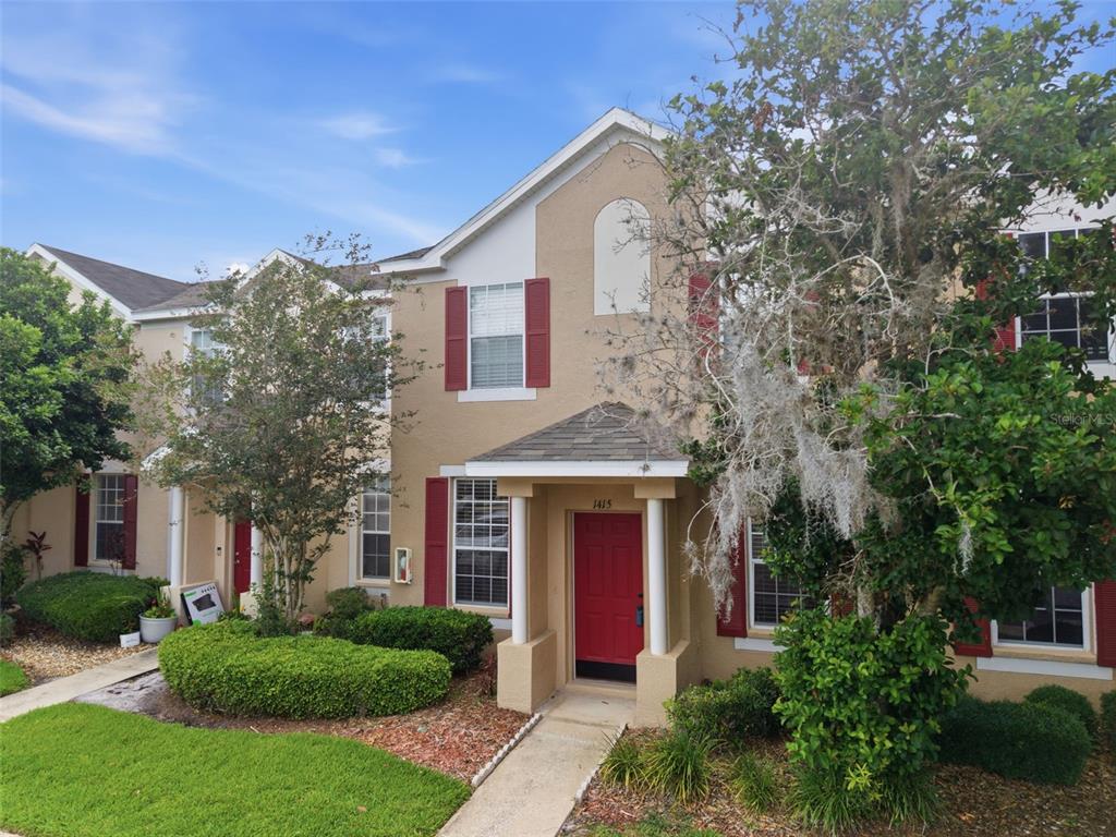 A two-story townhouse exterior with tan stucco walls, red shutters, and a red front door — 1415 SEDGWICK DRIVE, WESLEY CHAPEL, FL