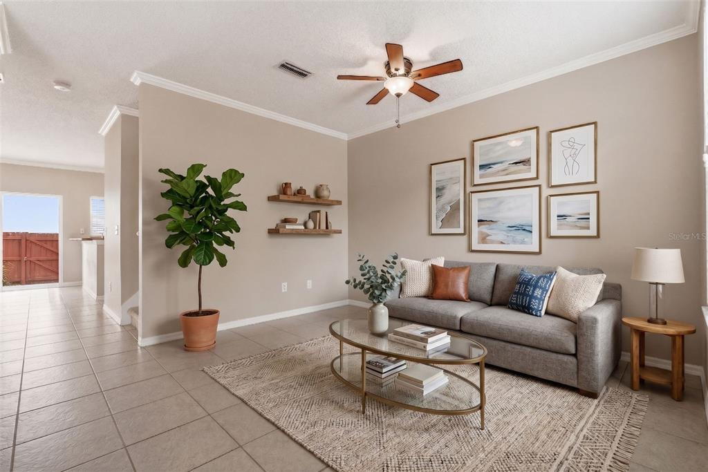 A living room features a grey sofa, glass coffee table, wall art, and a potted plant — 1415 SEDGWICK DRIVE, WESLEY CHAPEL, FL