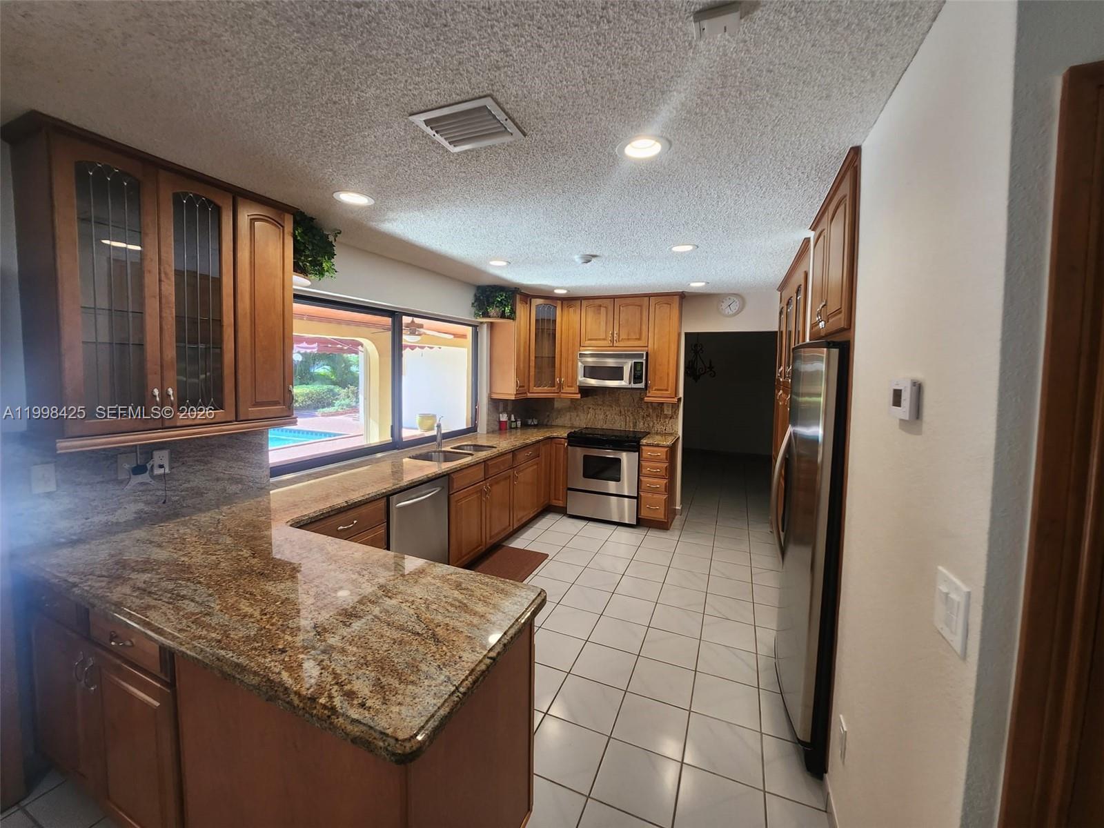 A kitchen features wood cabinets, granite countertops, stainless steel appliances, and tile flooring — 2980 SW 111th Ave, Miami FL 33165, MIAMI, FL