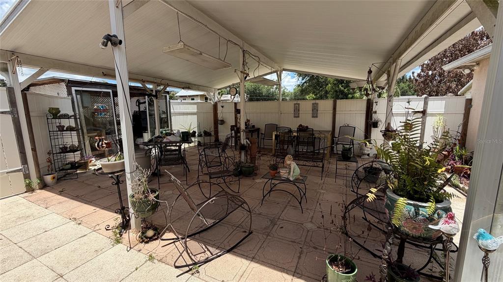 A covered outdoor patio features a tiled floor, various metal chairs, and numerous potted plants — 3690 WELLINGTON PLACE, BARTOW, FL
