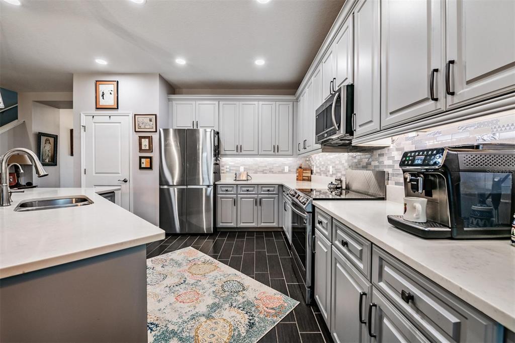 A kitchen features light gray cabinets, stainless steel appliances, white countertops, and dark tile flooring — 3920 NIGHT STAR TRAIL, ODESSA, FL