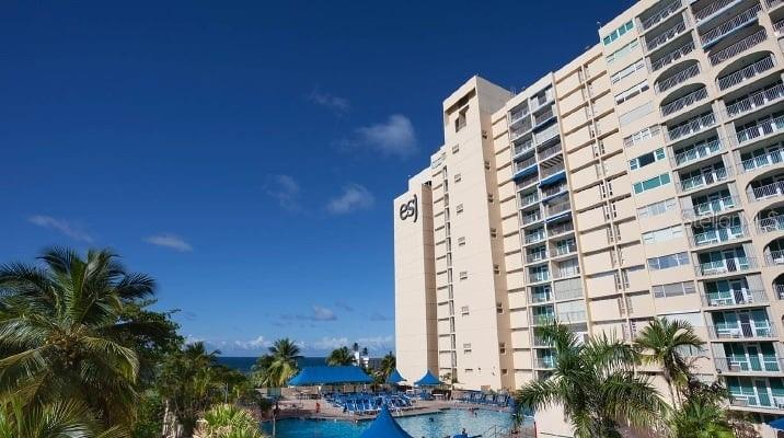 A tall, beige multi-story hotel building stands next to a swimming pool and palm trees — 6165 AVE. ISLA VERDE UNIT 369, CAROLINA, PR
