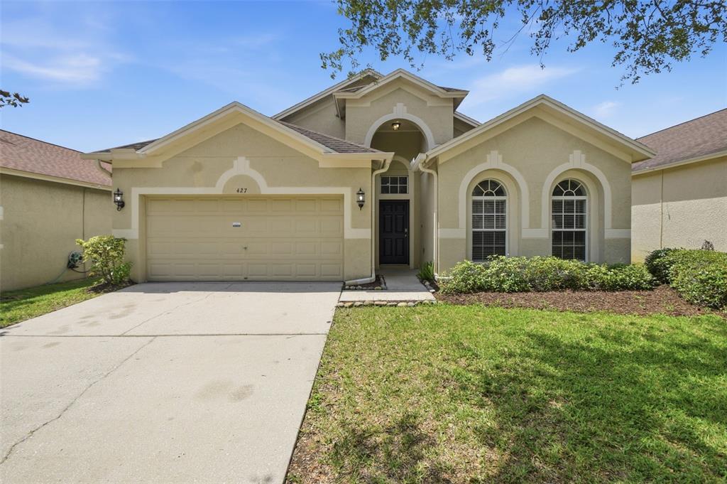 A single-story house with a beige stucco exterior, a two-car garage, and arched windows — 427 FERN GULLEY DRIVE, SEFFNER, FL