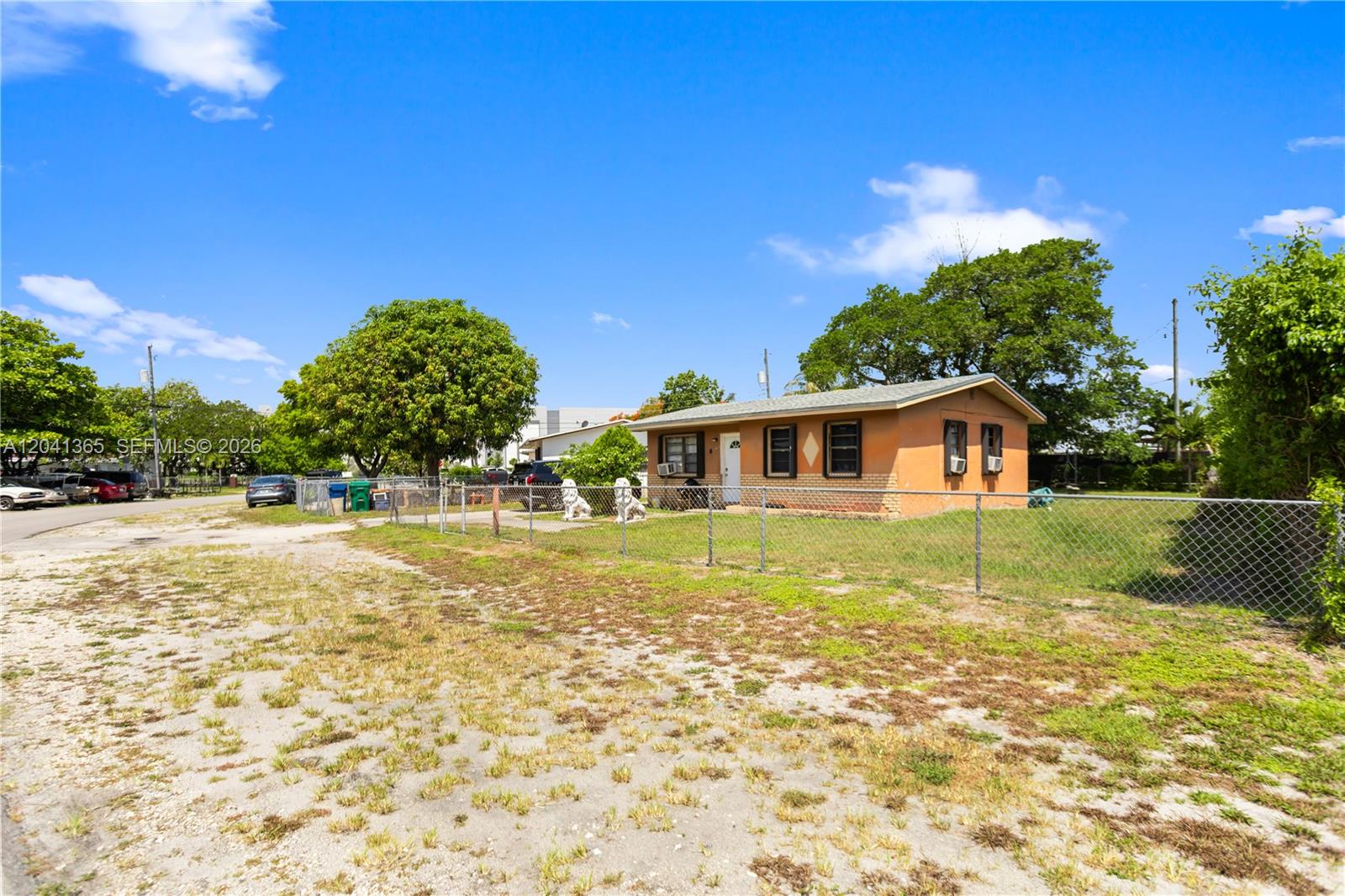 A single-story house with tan stucco walls sits behind a chain-link fence — 555 Harem Ave, Opa-Locka FL 33054, OPA-LOCKA, FL