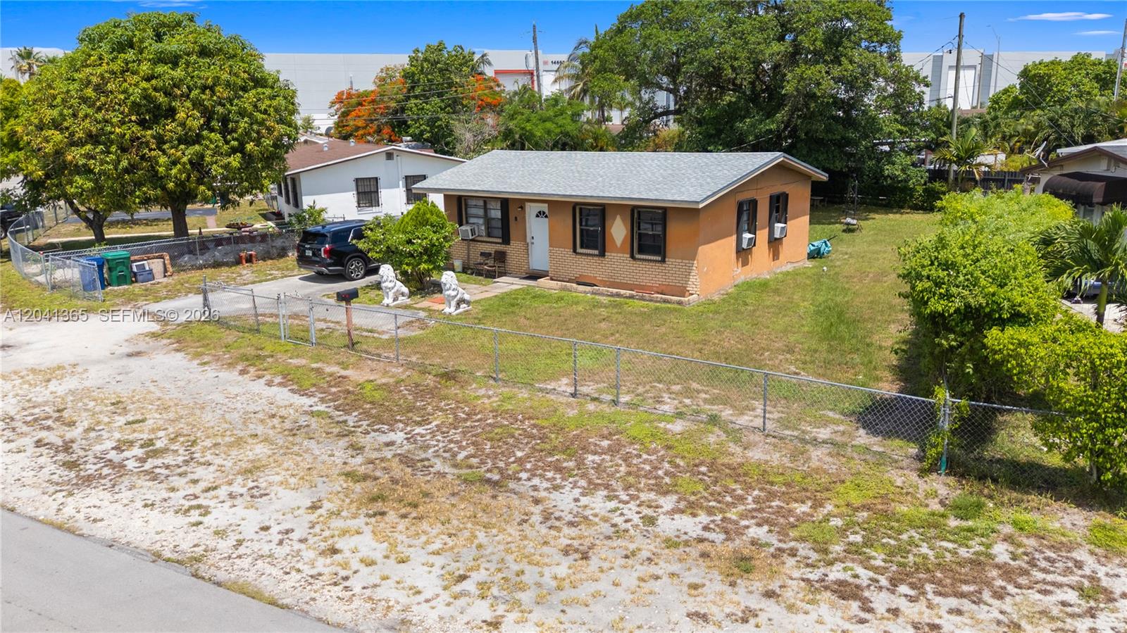 An exterior view of a single-story house with a chain-link fence and two lion statues — 555 Harem Ave, Opa-Locka FL 33054, OPA-LOCKA, FL