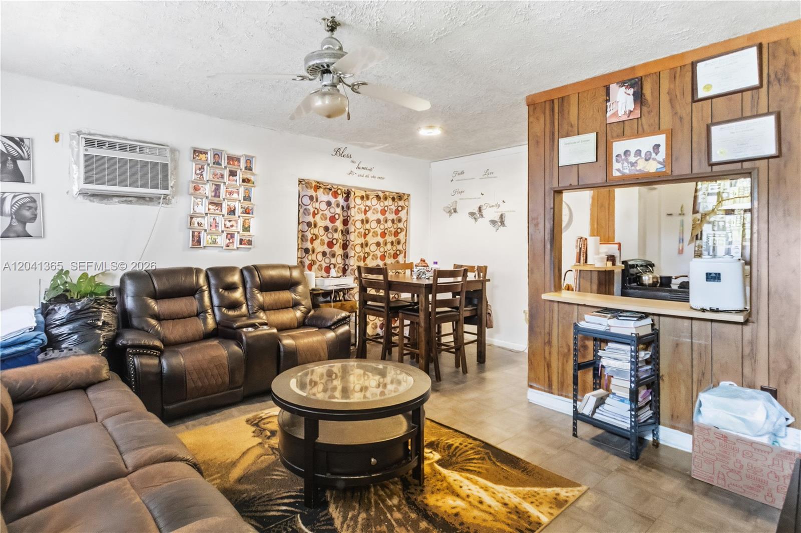 A living room with brown leather furniture, a dining set, and wood-paneled kitchen pass-through wall — 555 Harem Ave, Opa-Locka FL 33054, OPA-LOCKA, FL