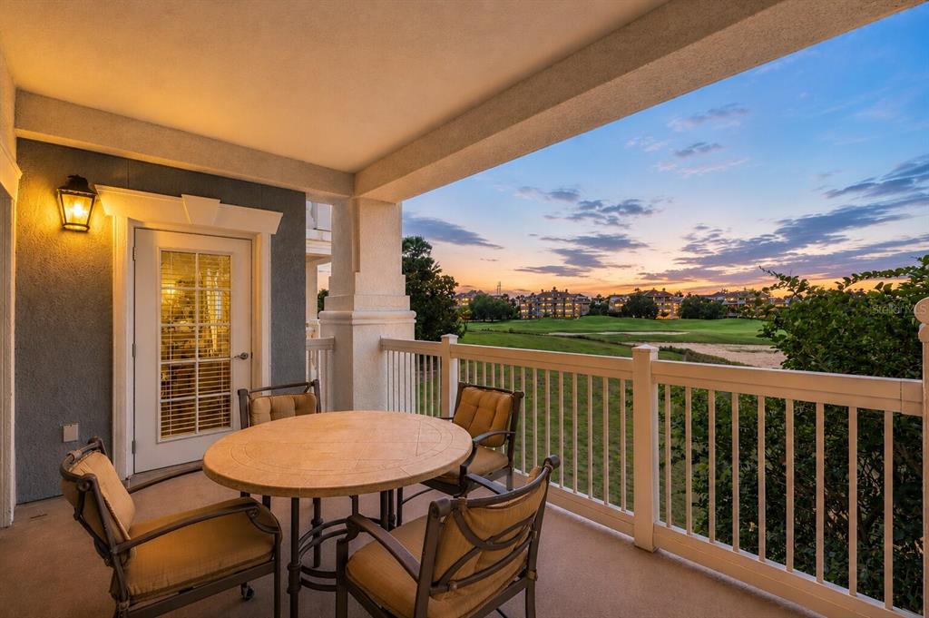 A covered balcony features a round table with four chairs overlooking a golf course at sunset — 1100 SUNSET VIEW CIRCLE UNIT 204, REUNION, FL