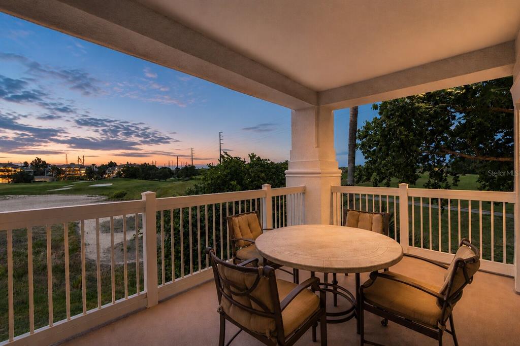 A covered balcony features a round stone table with four chairs overlooking a golf course — 1100 SUNSET VIEW CIRCLE UNIT 204, REUNION, FL