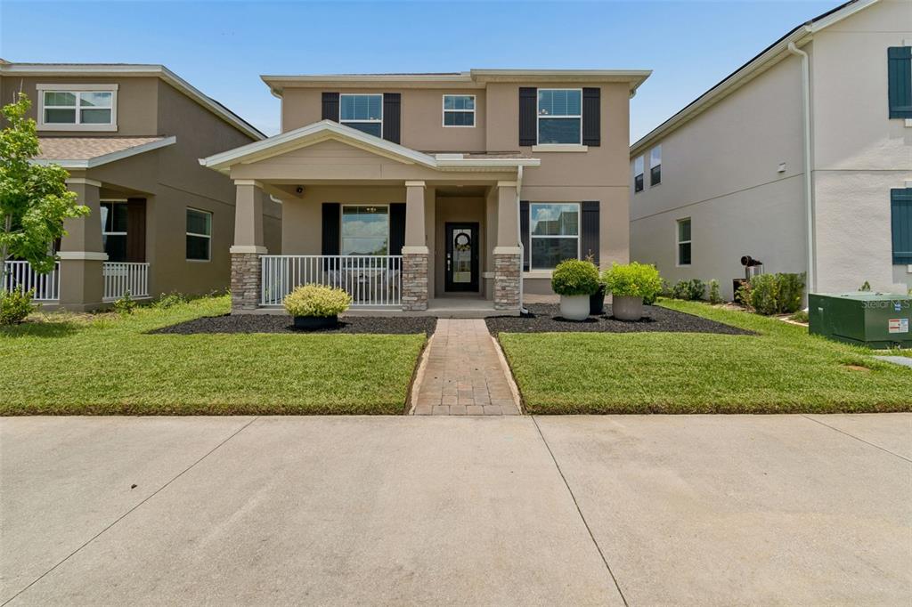 A two-story suburban house with a covered front porch, stone accents, and a paved walkway — 9745 INTRODUCTION WAY, ORLANDO, FL