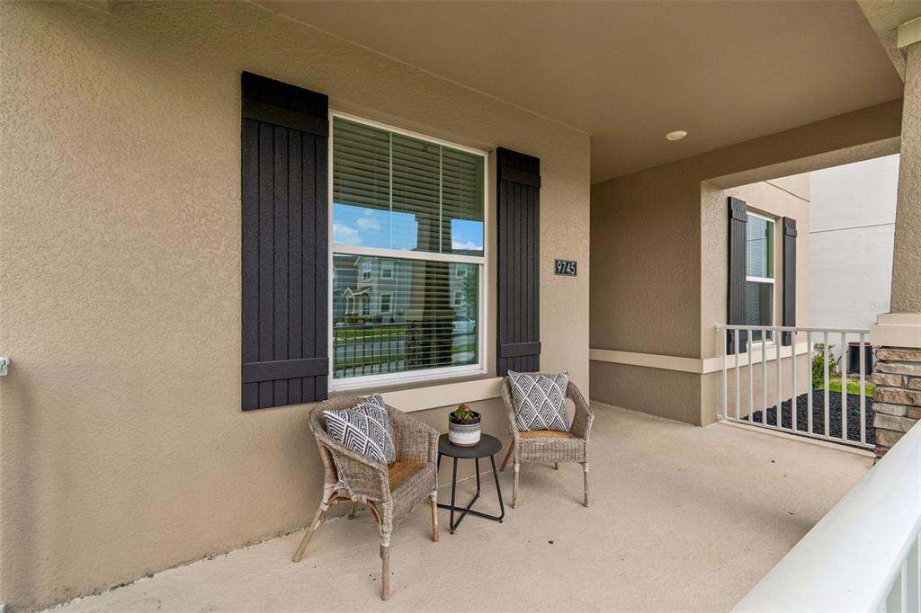 A covered porch features two wicker chairs, a small side table, and a window with shutters — 9745 INTRODUCTION WAY, ORLANDO, FL