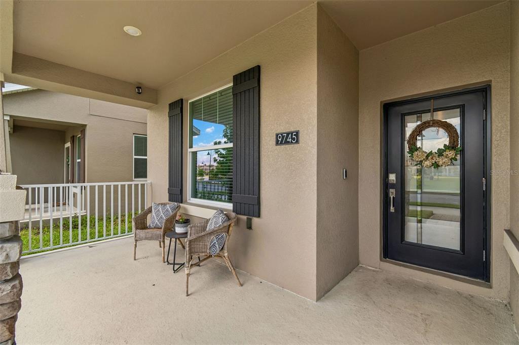 A covered front porch features two wicker chairs, a small table, and a glass-paneled door — 9745 INTRODUCTION WAY, ORLANDO, FL