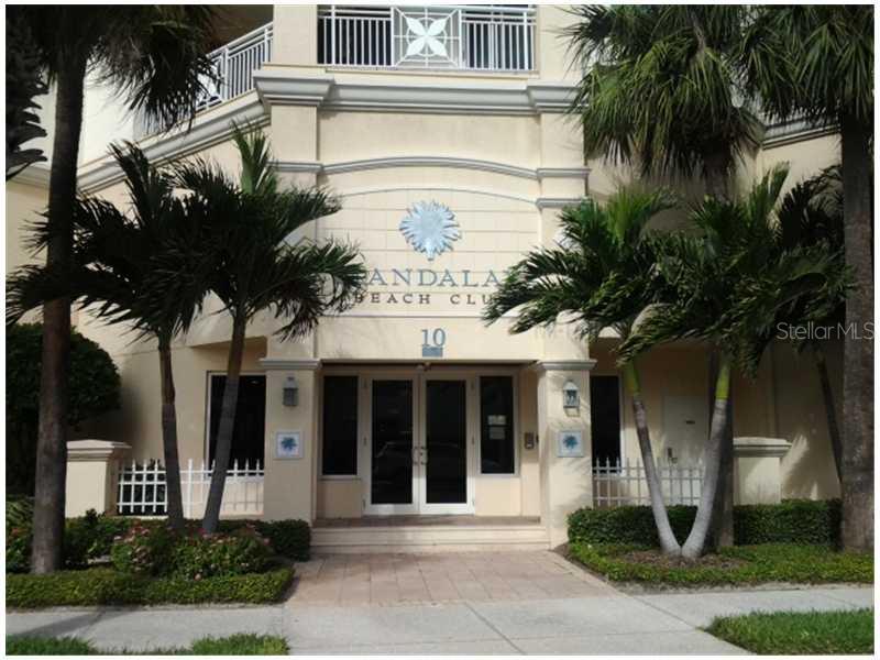 The exterior entrance of a building features palm trees, a white fence, and glass doors — 11 SAN MARCO STREET UNIT 1206, CLEARWATER, FL