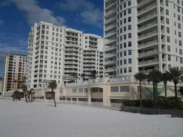 A multi-story residential building with balconies stands behind a wide, sandy beach — 11 SAN MARCO STREET UNIT 1206, CLEARWATER, FL