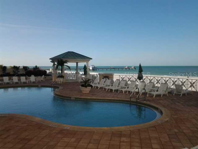 A swimming pool sits on a patio overlooking a beach with a pier and gazebo — 11 SAN MARCO STREET UNIT 1206, CLEARWATER, FL