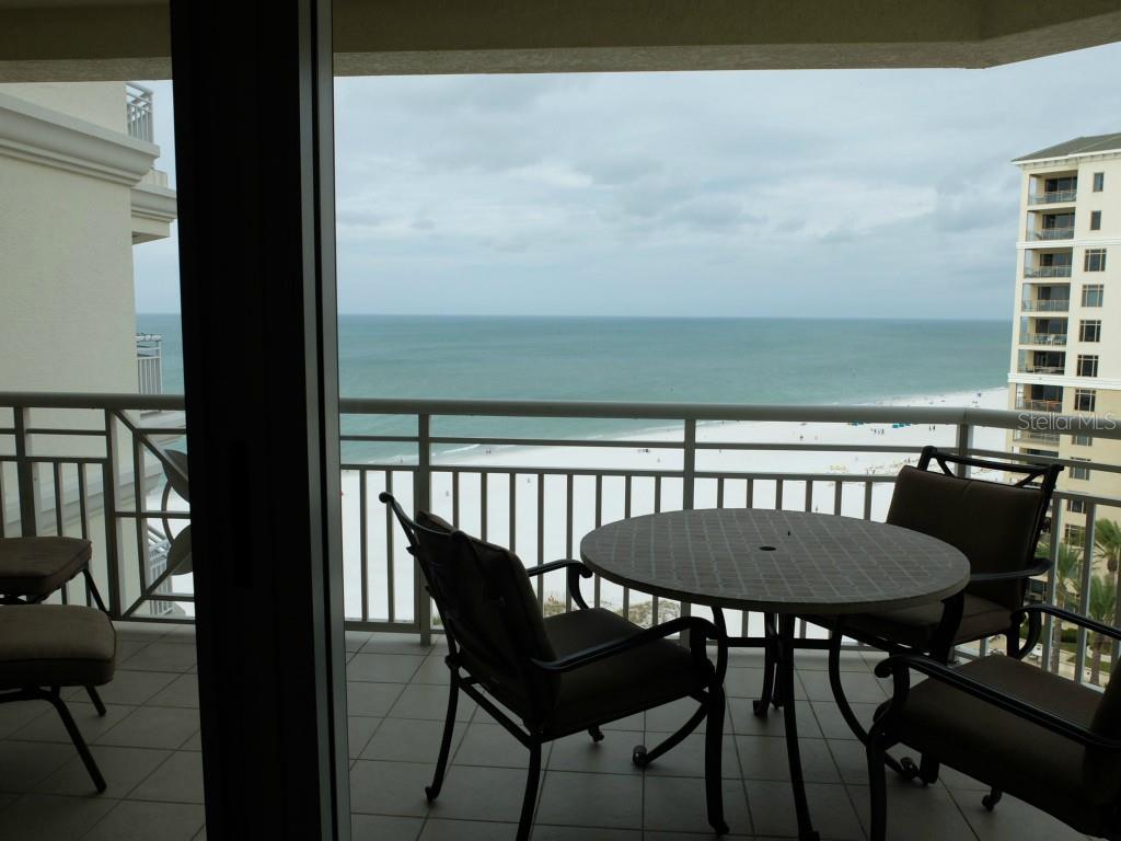 A balcony with patio furniture overlooks a sandy beach and the ocean under a cloudy sky — 11 SAN MARCO STREET UNIT 1206, CLEARWATER, FL