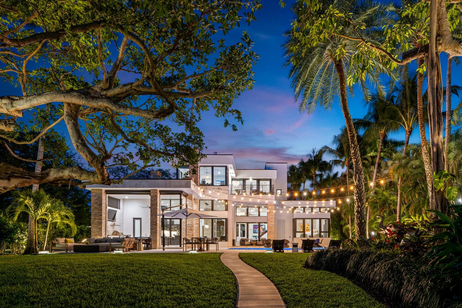 A modern multi-story house with a pool, patio, and string lights at twilight — 1080 Lake Drive, Delray Beach FL 33444, DELRAY BEACH, FL