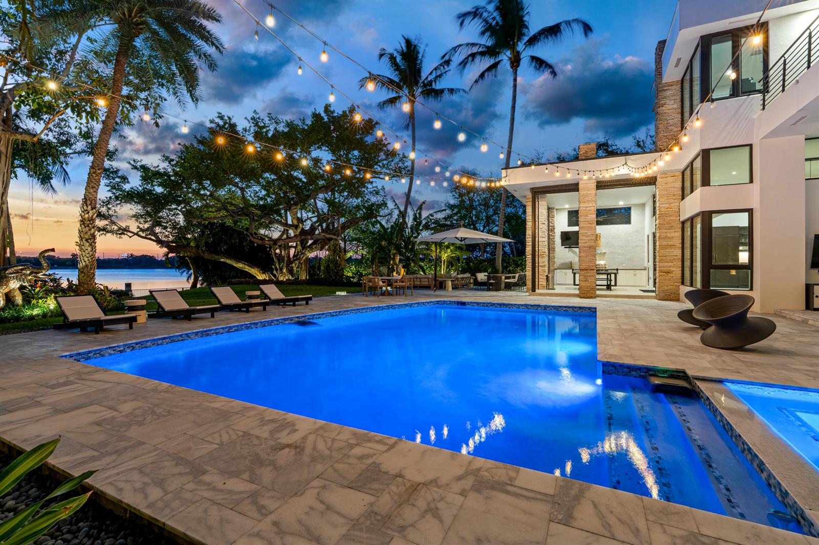 A modern house with a pool, patio, string lights, and palm trees at sunset — 1080 Lake Drive, Delray Beach FL 33444, DELRAY BEACH, FL