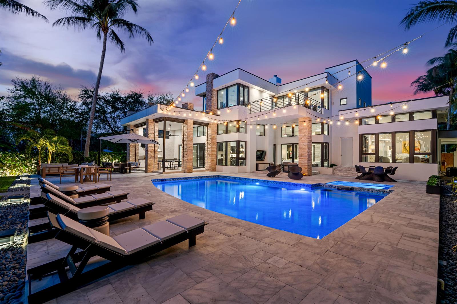 A modern two-story house with a swimming pool, patio, and string lights at dusk — 1080 Lake Drive, Delray Beach FL 33444, DELRAY BEACH, FL