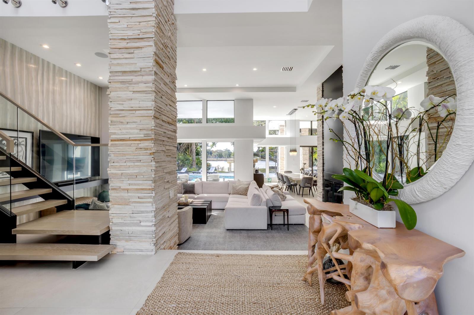 A modern open-concept living area features a stone pillar, floating staircase, and a large mirror — 1080 Lake Drive, Delray Beach FL 33444, DELRAY BEACH, FL