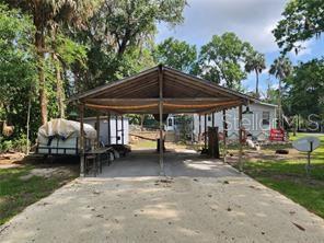 A gravel driveway leads to a large wooden carport structure in a wooded residential yard — 5550 S CORAL BELLS AVENUE, HOMOSASSA, FL