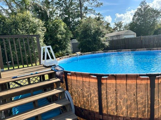 An above-ground swimming pool with a wooden deck and stairs sits in a backyard — 4090 SW 167TH STREET, OCALA, FL