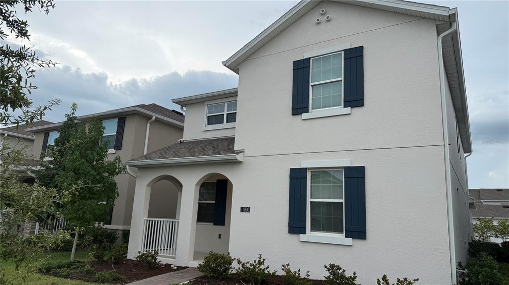 A two-story house with light-colored stucco walls, dark blue shutters, and a covered front porch — 11830 LANGUAGE WAY, ORLANDO, FL