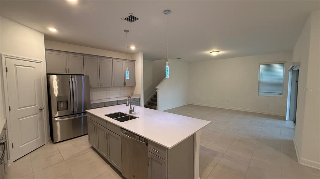 A kitchen with gray cabinets, a white island, and stainless steel appliances opens to a living area — 11830 LANGUAGE WAY, ORLANDO, FL