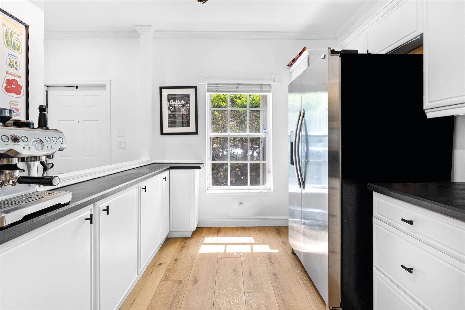 A kitchen features white cabinets, black countertops, a stainless steel refrigerator, and a window — 809 Kokomo Key Lane, Delray Beach FL 33483, DELRAY BEACH, FL
