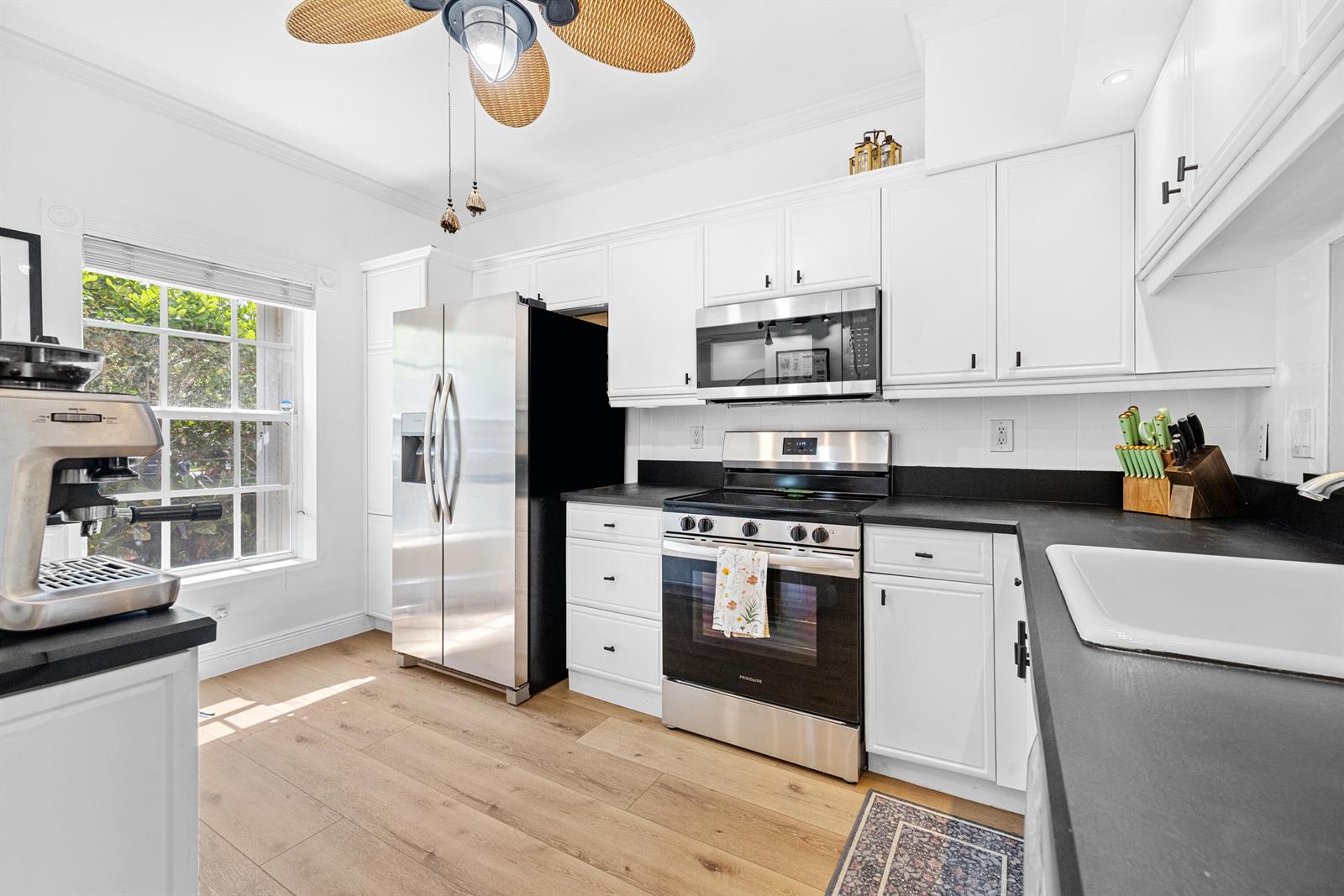 A kitchen features white cabinets, stainless steel appliances, black countertops, and light wood flooring — 809 Kokomo Key Lane, Delray Beach FL 33483, DELRAY BEACH, FL