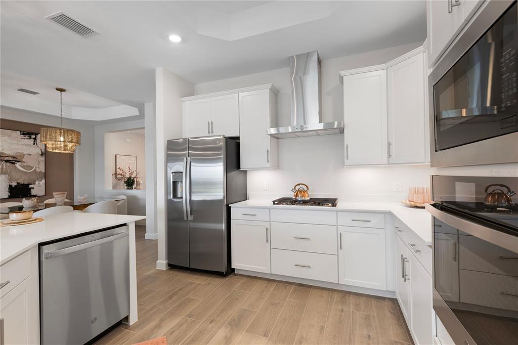 A modern kitchen features white cabinetry, stainless steel appliances, and wood-look tile flooring — 19718 TROUT TERRACE, LAKEWOOD RANCH, FL