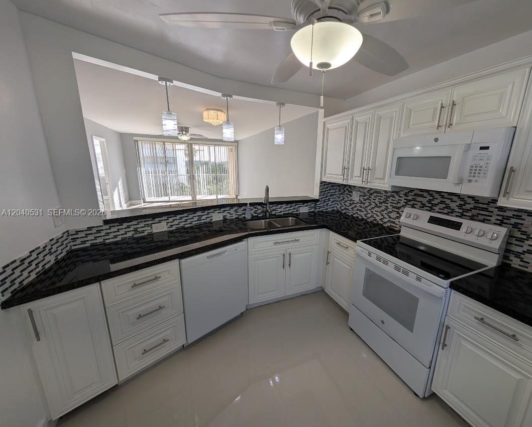 A kitchen features white cabinets, black countertops, a tiled backsplash, and a pass-through window — 1750 NE 191st St # 3, Miami FL 33179, MIAMI, FL