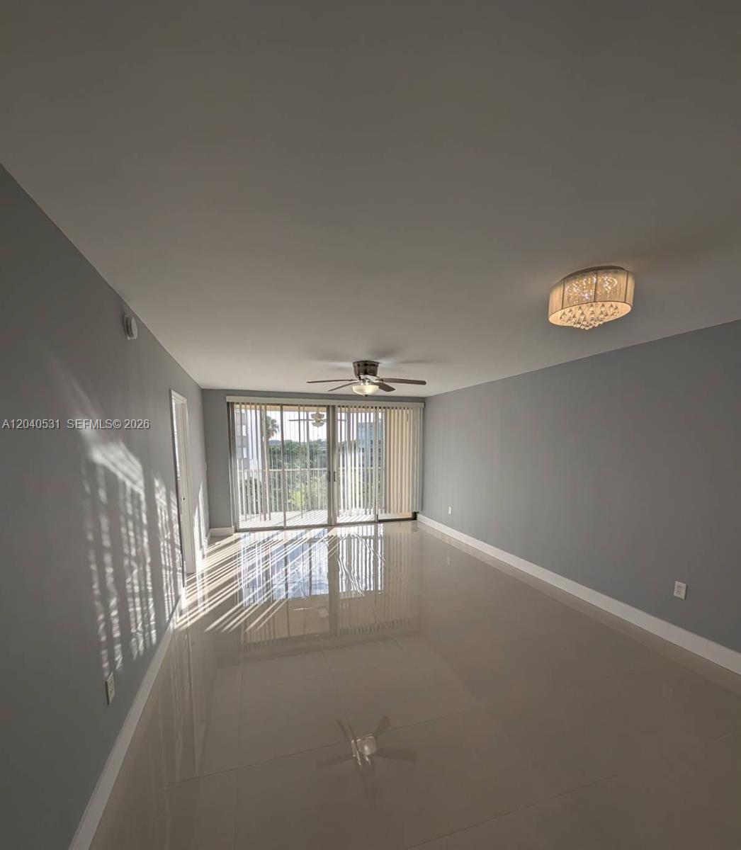 An empty living room features light gray walls, large glossy floor tiles, and a balcony — 1750 NE 191st St # 3, Miami FL 33179, MIAMI, FL