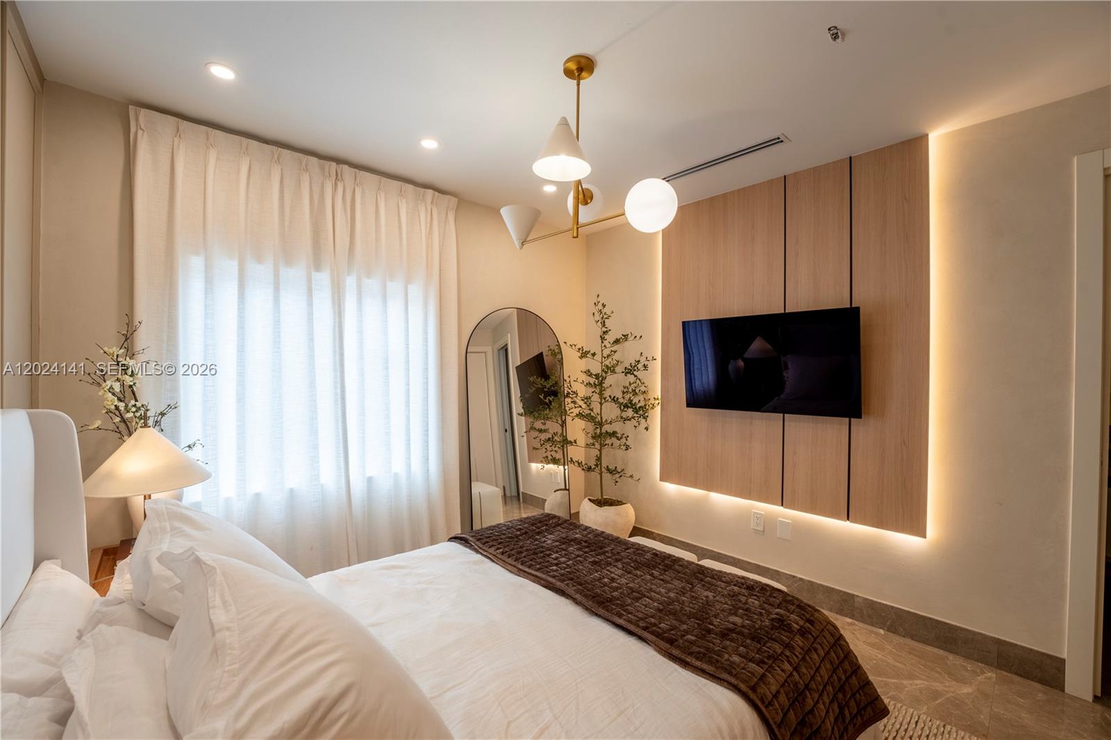 A modern bedroom features a wall-mounted television on a wood-paneled accent wall with backlighting — DORAL, FL