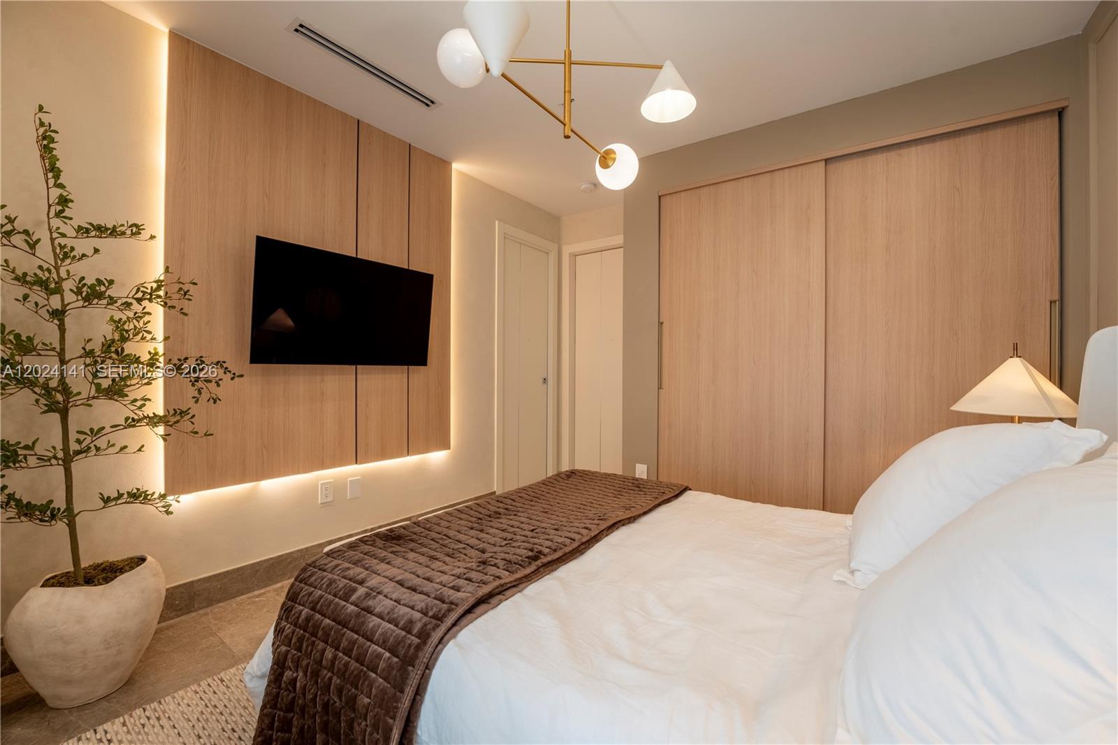 A bedroom features a wood-paneled accent wall with a mounted television and integrated lighting — DORAL, FL